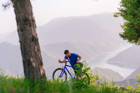 Mountain biker wearing a blue shirt is pushing his bike through green woods while enjoying the...