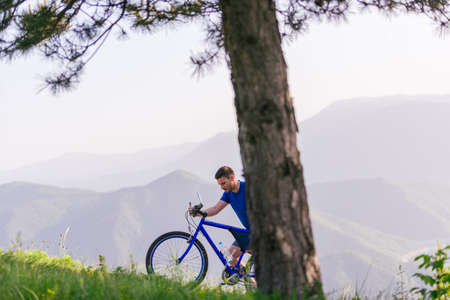 Mountain biker wearing a blue shirt is pushing his bike through green woods while enjoying the amazing view.の写真素材