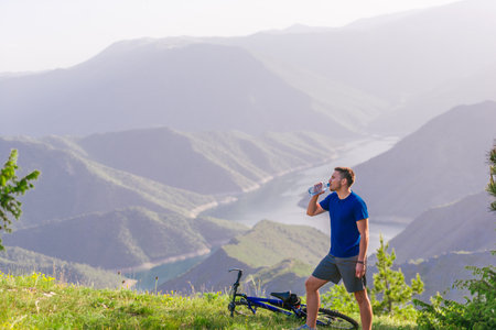 Mountain biker drinks water while standing at a green valley and having some rest.の写真素材