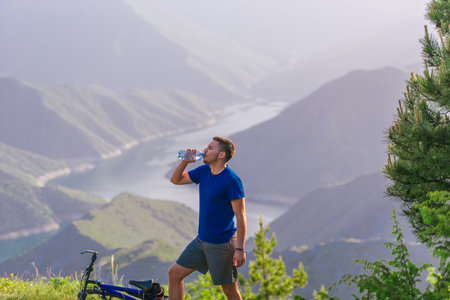Mountain biker drinks water while standing at a green valley and having some rest.の写真素材