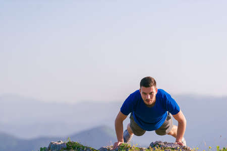 Fit male athlete doing pushups at the edge of a cliff while enjoying the amazing view.