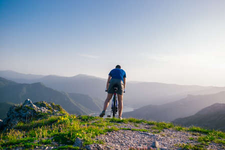 Adventurous Cyclist riding his mountain bike at the edge of a cliff, on rocky terrain while wearing no safety equipment.Amazing top view.の写真素材