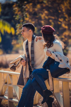 Beautiful couple is sitting on the bridge in the park and enjoying the autumn day togetherの写真素材