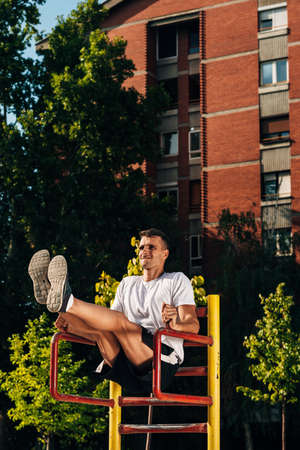Young muscular build man doing dips exercises on horizontal bar outdoors