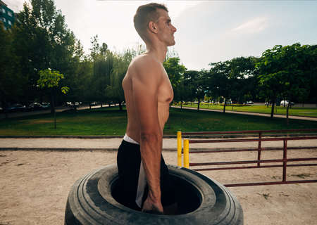 Shitless sportsman lifting tire during cross training in outdoors gym
