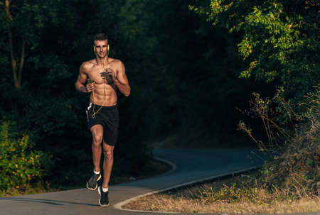 Fit crossfit man spint in mountain path while listen music on his cellphone