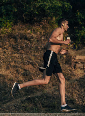 Man jogging with headphones while sprinting on road in mountains