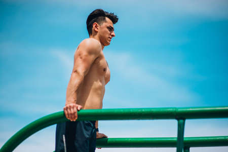 Fitness, sport, exercising, training and lifestyle concept - young man doing triceps dip on parallel...