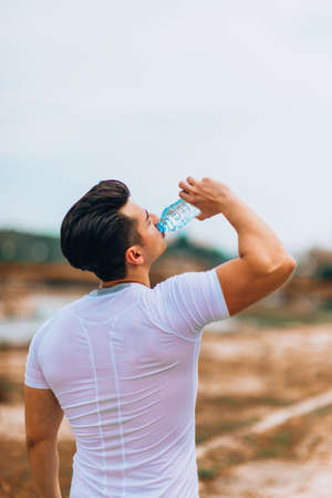 Athletic sport man drinking water from a bottle. Cold drink after outdoor fitnessの写真素材