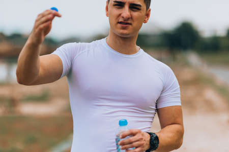 Attractive young man resting and drinking some water after exercising outdoors in the park