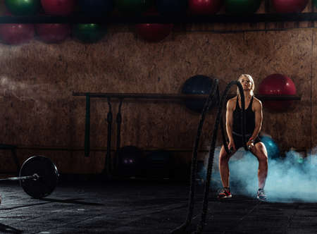 Attractive muscular woman working out with heavy ropes in crossfit center