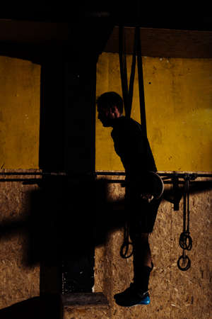 Silhouette male at functional fitness training in gym doing sport on rings