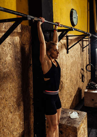 Pretty young brunette working out and doing some pull ups at a crossfit gym