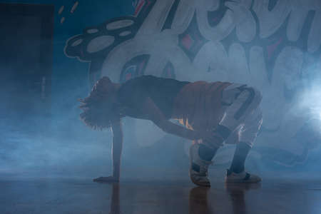 Young man break dancing in club with lights and smoke.