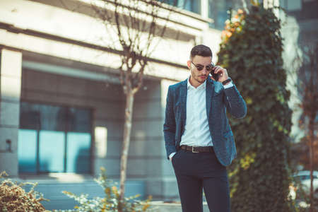Suit man is standing in urban city square, looking nervious while talking on the phoneの写真素材