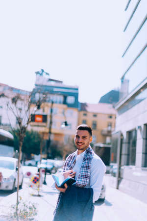 Cheerful businessman is having fun while drinking his coffee on the street and looking at his...