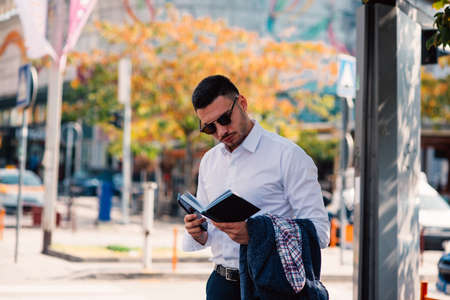 Handsome businessman is in the city, talking and walking on the street, holding notebook in his hands.の写真素材