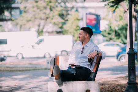 Urban businessman is sitting on the bench in the city center,smiling and relaxing after the long hard day.の写真素材