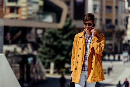 Confident businessman holding briefcase and talking on cellphone in city center