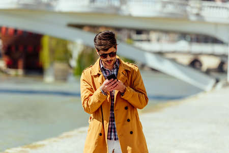 Handsome young businessman using his smartphone near the city riverの写真素材