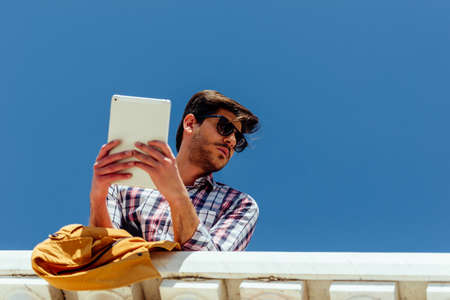 Urban businessman using PC tablet against blue skyの写真素材