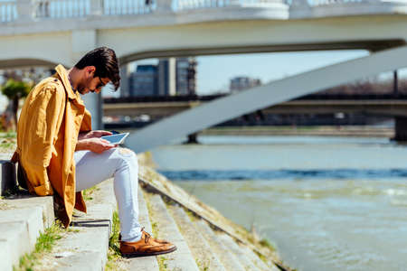 Young man typing text message on his tablet and enjoying in sunny dayの写真素材