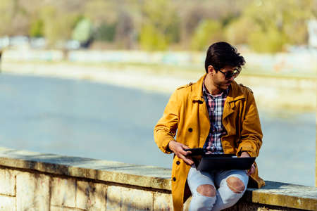 Businessman using his laptop for work while sitting near river