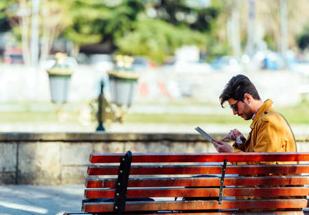 Modern businessman is sitting on a bench and looking at the tabletの写真素材