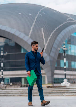 Cheerful businessman wearing glasses having a phone conversation standing in his office in downtownの写真素材