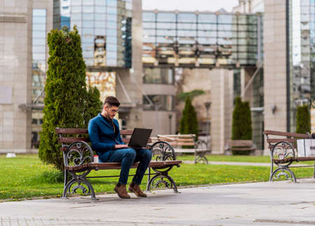Stylish man in blue suit using laptop for work and drinking coffee in the park