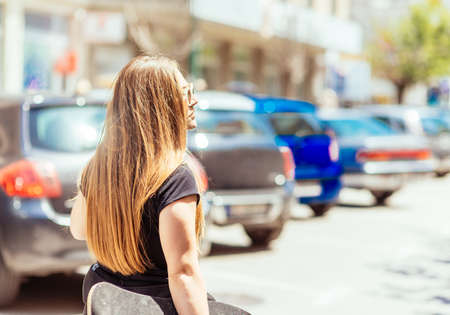 Back view of beautiful young girl with skateboard outdoors on a hot summer dayの写真素材