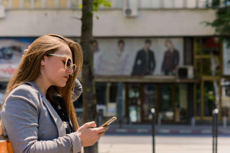 Woman sitting and using a smart phone at the street in a sunny summer dayの写真素材