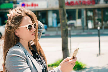 Woman walking and using a smart phone in the street in a sunny summer dayの写真素材