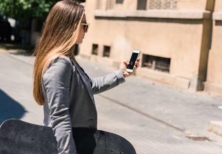 Back view of a fashion woman walking and using a smart phone on a city street