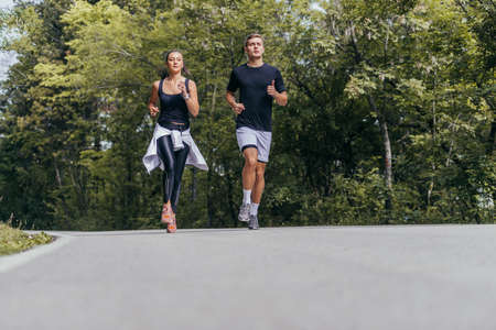 Young fit couple atheltes running on running road in a forest.の写真素材