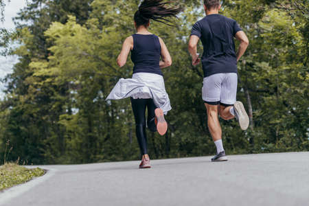 Young fit couple atheltes running on running road in a forest.の写真素材