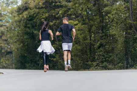 Young fit couple atheltes running on running road in a forest.の写真素材