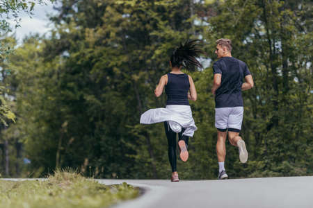 Young fit couple atheltes running on running road in a forest.の写真素材