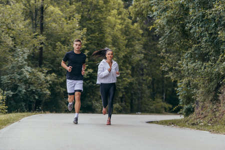 Athletic couple running on a street next to each other. Nature,fit and healthy concept.の写真素材