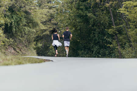 Young fit couple atheltes running on running road in a forest.