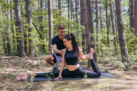 Young active couple doing stretching exercises in the woods on a yoga mat after jogging and running