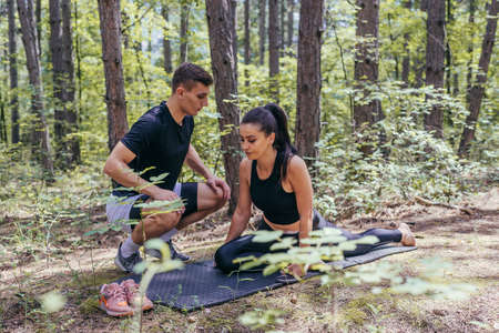 A beautiful young fitness couple is preparing for stretching before running in the forest.の写真素材