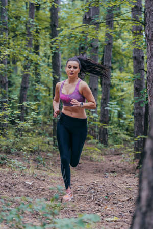 Young athletic sporty girl is jogging outside on a forest pathの写真素材