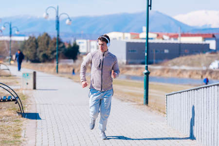 A panting athlete running fast on a track while wearing headphones and grey sweatpants, early in the morning on a sunny day.の写真素材