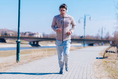 A panting athlete running fast on a track while wearing headphones and grey sweatpants, early in the morning on a sunny day.の写真素材