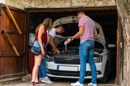 Two guys trying to fix some car troble while a girl is standing next to themの写真素材