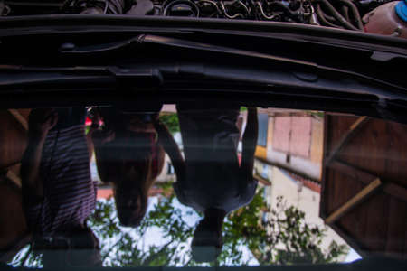 Refflection on the window of three people who are discussing with opened hood on their carの写真素材