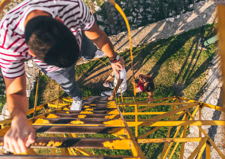 A guy is climbing on iron construction, looking down and talking to his friendの写真素材