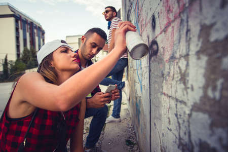 A girl is with her two friends outdoors, writing letteres on old wallの写真素材