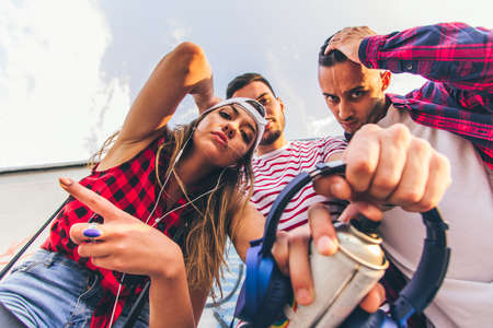 Three friends are together, looking down and holding headphones and sprayの写真素材